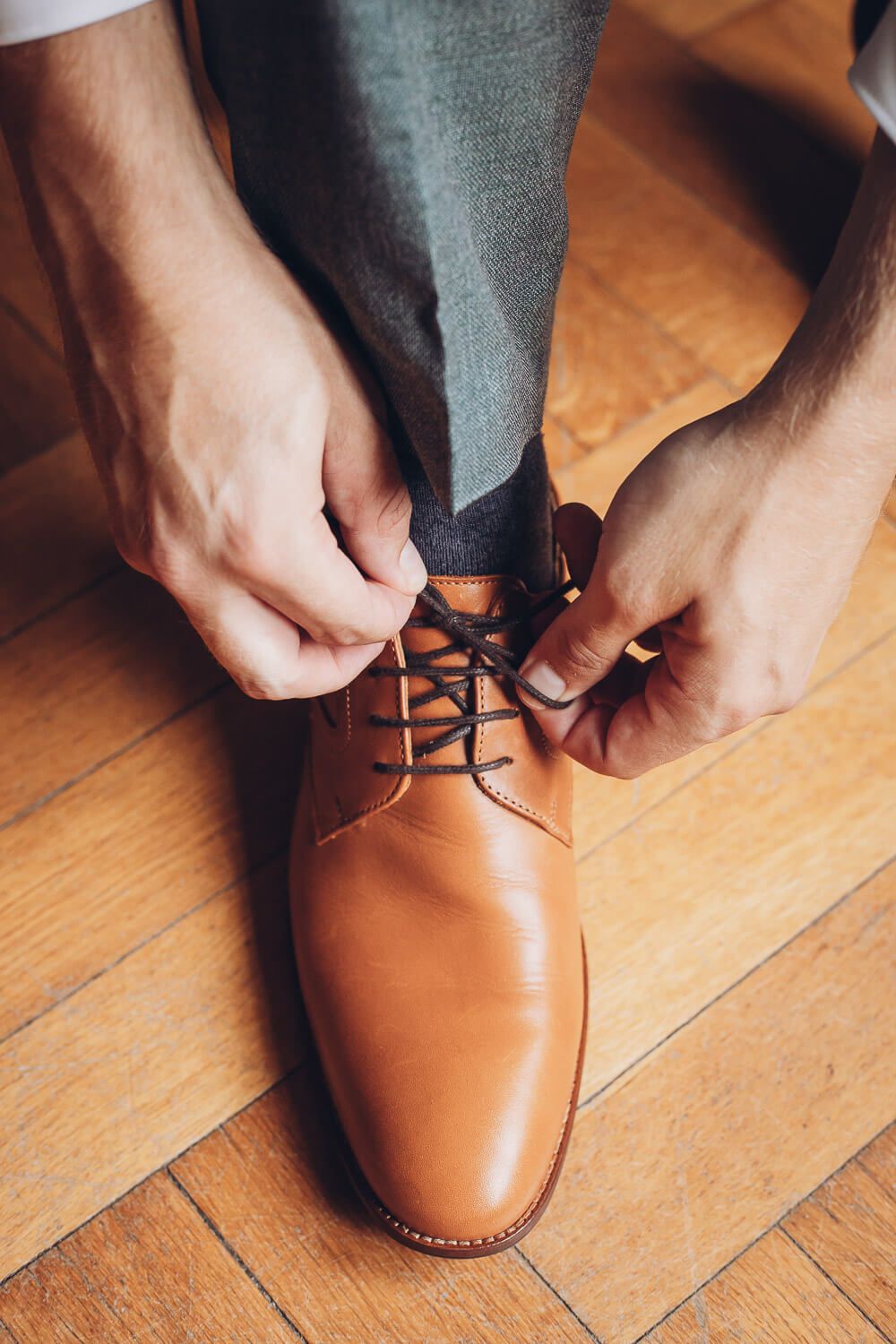 Detailaufnahme eines Bräutigams beim Binden seiner braunen Lederschuhe am Hochzeitstag, fotografiert von einem Fotografen in Gehrden
