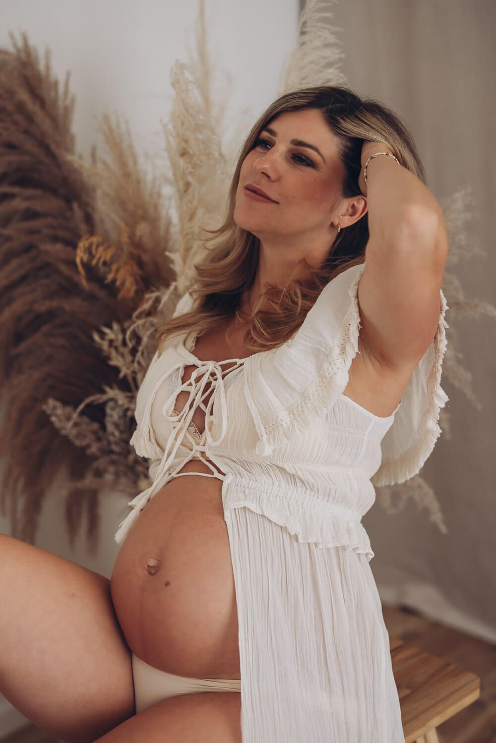 Stilvolles Babybauch Fotoshooting in Celle – schwangere Frau im Boho Stil sitzt entspannt und blickt verträumt zur Seite