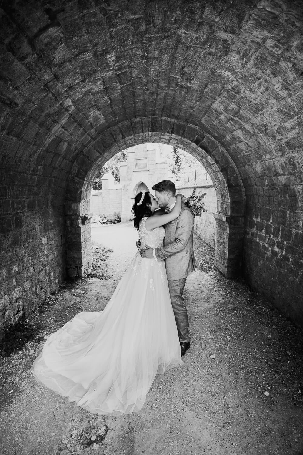 Schwarz-Weiß-Foto eines innigen Brautpaarmoments unter einem historischen Steinbogen an der Schloss Marienburg - Hochzeitsfotograf Minden