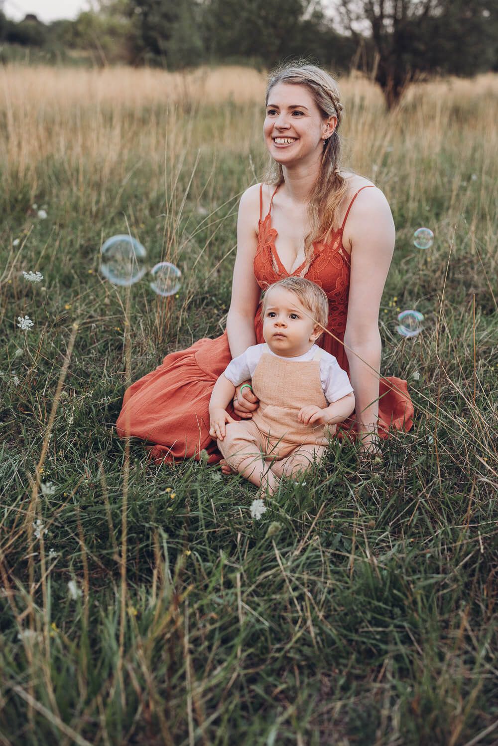 Mutter sitzt mit ihrem Baby auf einer Wiese während Seifenblasen durch die Luft fliegen beim Outdoor Shooting Hameln