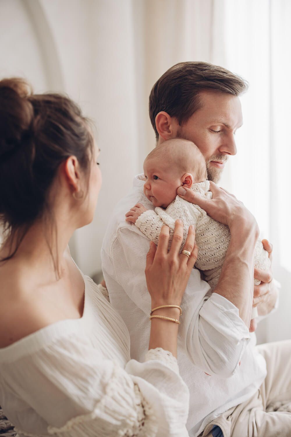 Vater hält sein Neugeborenes liebevoll auf der Schulter während die Mutter zusieht – natürliche Neugeborenenfotografie in Hannover und Umgeb
