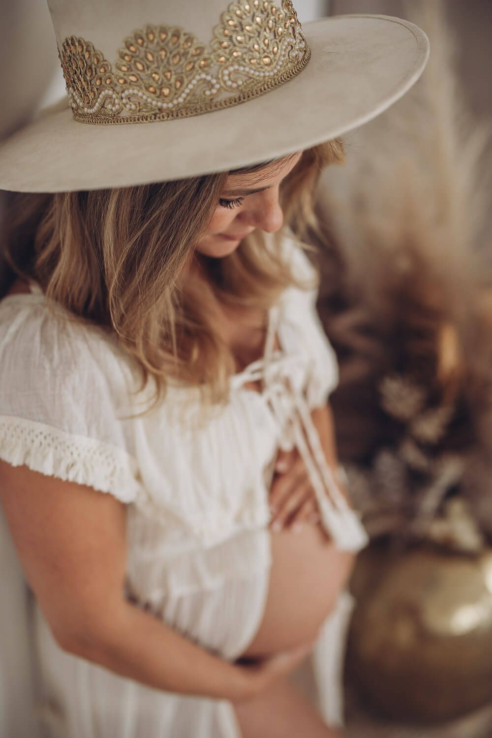 Detailaufnahme beim Babybauch Fotoshooting in Hannover – schwangere Frau mit Boho Hut blickt liebevoll auf ihren Babybauch