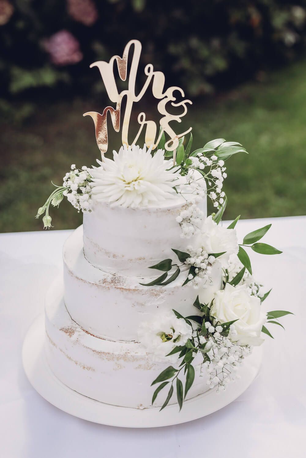 Elegante mehrstöckige Hochzeitstorte mit weißen Blumen und Mr-and-Mrs-Topper, fotografiert von einer Hochzeitsfotografin in Hannover