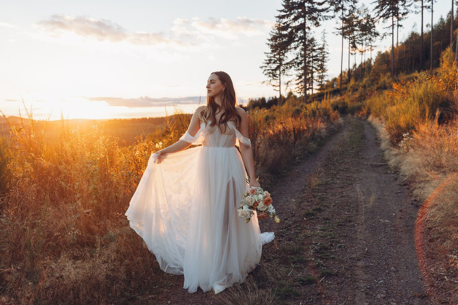 Braut steht allein im goldenen Sonnenuntergang auf einem Naturweg mit Brautstrauß bei einem Hochzeitsshooting in Wolfsburg und Hannover
