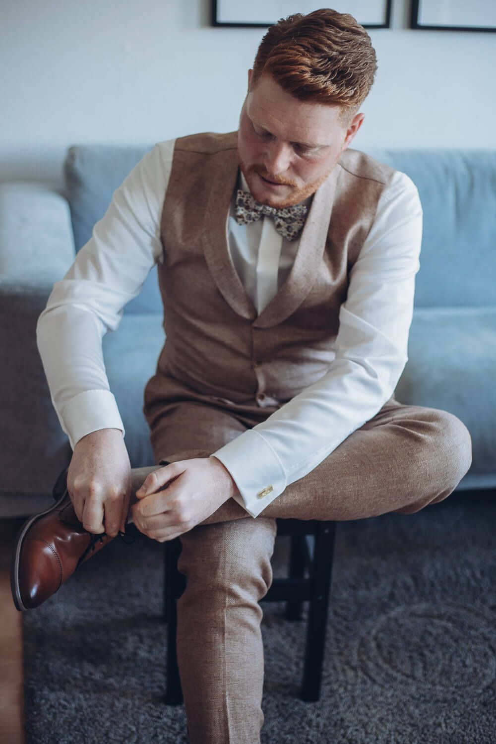 Bräutigam bindet sich beim Getting Ready konzentriert die Lederschuhe, fotografisch begleitet von einem Hochzeitsfotografen vor der Hochzeit