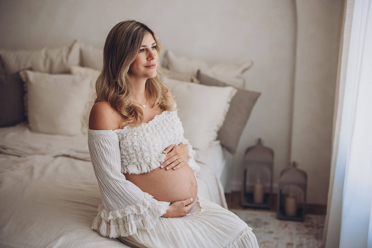 Babybauch Fotoshooting in Hameln – schwangere Frau sitzt auf dem Bett und umfasst ihren Bauch mit beiden Händen