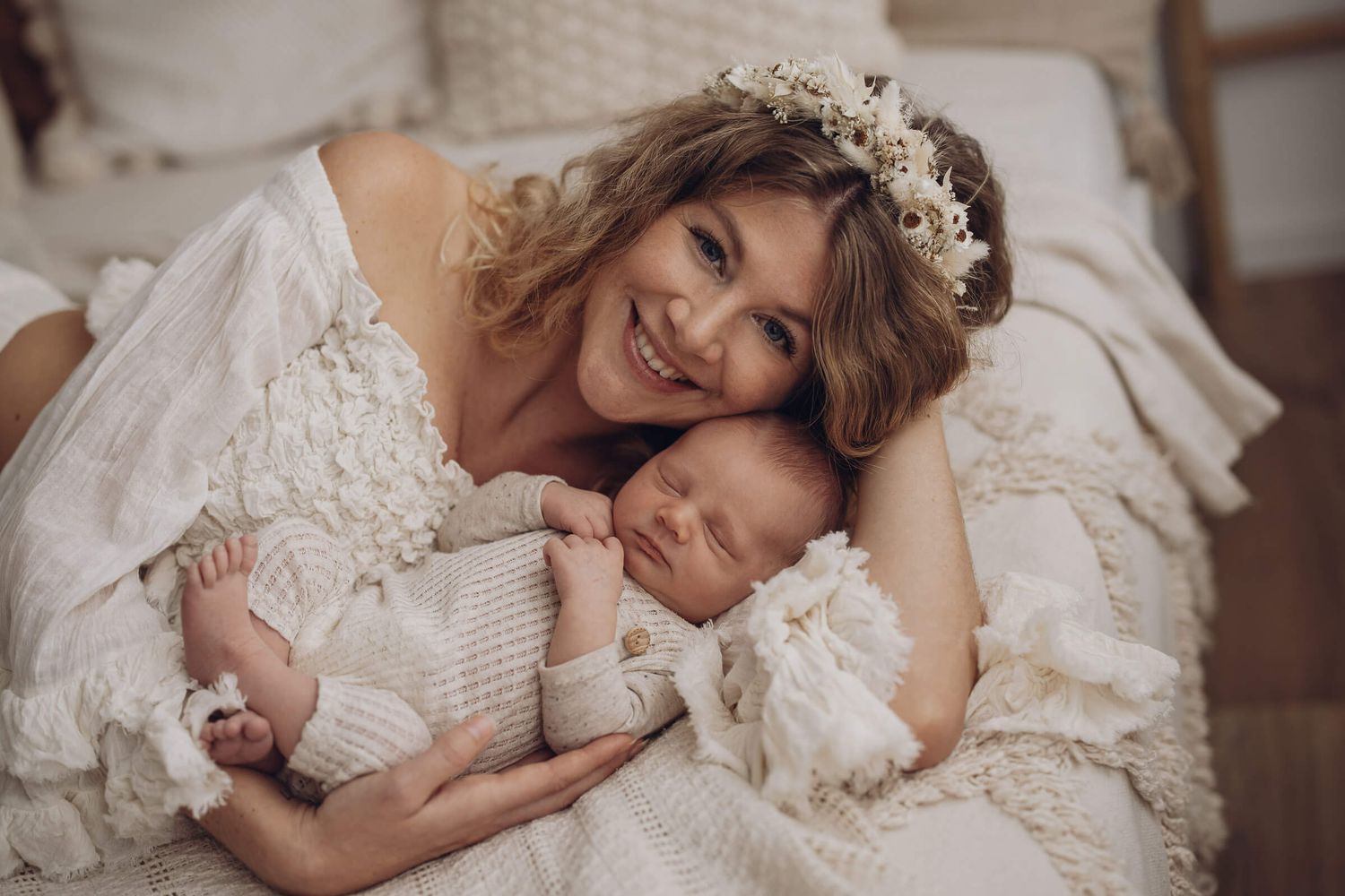 Glückliche Mutter liegt mit ihrem neugeborenen Baby auf einem Bett – natürliche und emotionale Babyfotografie im hellen, warmen Stil