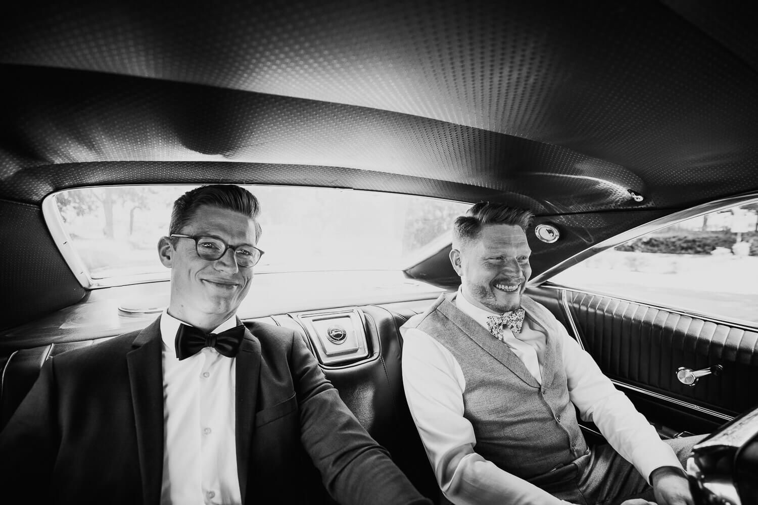 Bräutigam und Trauzeuge sitzen gut gelaunt im Oldtimer bei einer Hochzeit in Minden, festgehalten von einem Hochzeitsfotografen