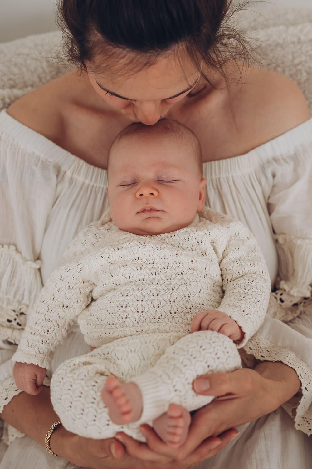 Liebevolle Mutter hält ihr schlafendes Baby im Fotostudio Hannover und gibt ihm einen sanften Kuss auf den Kopf