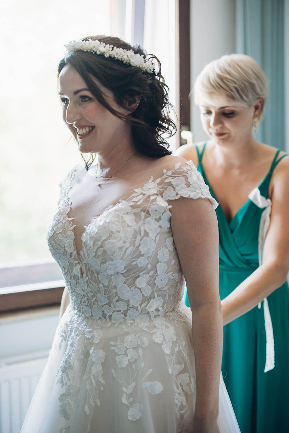 Getting Ready der Braut in Garbsen: Eine Begleitperson hilft ihr vor der freien Trauung in das Brautkleid - Hochzeitsfotograf