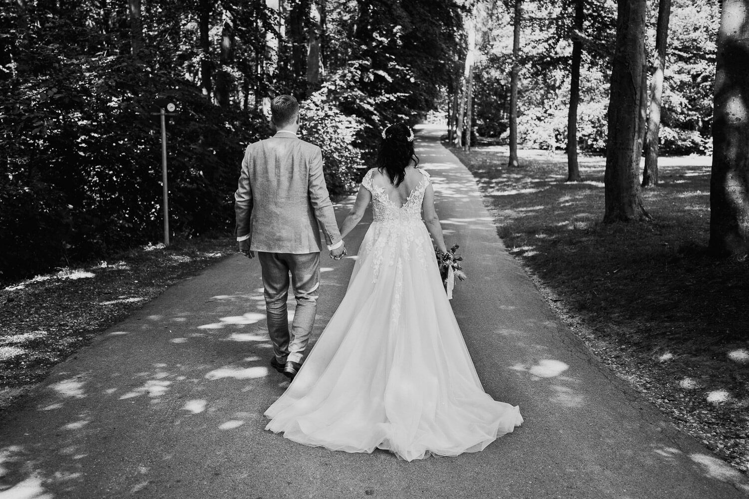 Das Brautpaar geht Hand in Hand über einen von Bäumen gesäumten Weg, fotografiert in Schwarz-Weiß - Hochzeitsfotografin Hildesheim