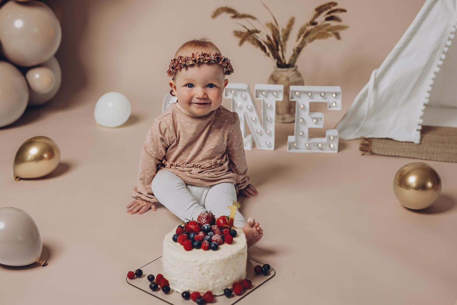 Baby sitzt vor einer Torte beim Cake Smash Fotoshooting zum ersten Geburtstag in einem liebevoll dekorierten Fotostudio
