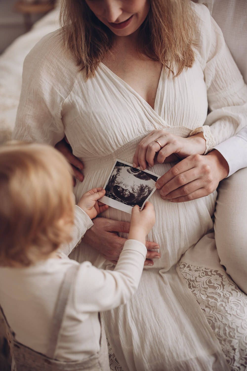 Kind hält Ultraschallbild vor den Babybauch der Mutter als emotionale Familienaufnahme