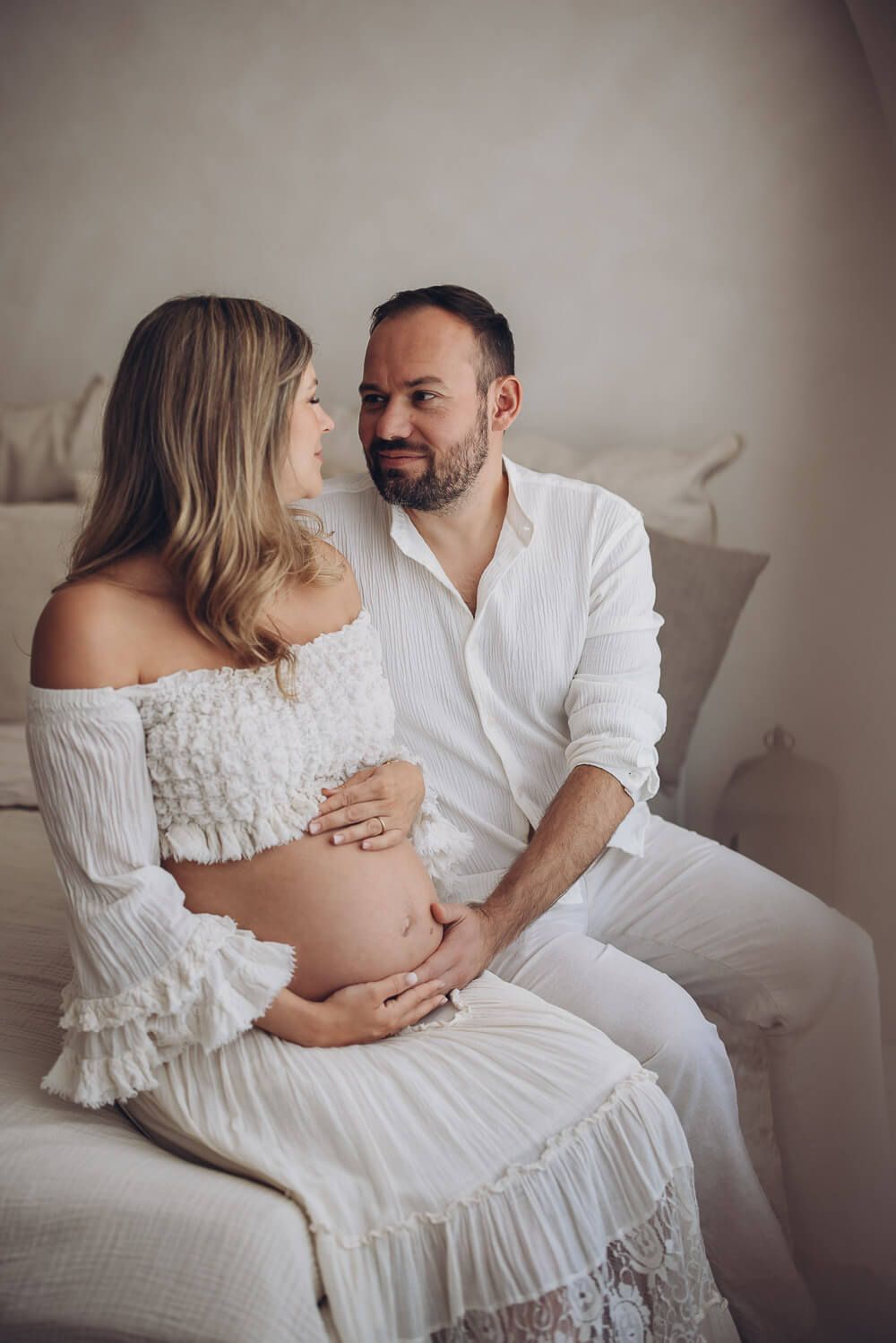 Harmonisches Babybauch Fotoshooting in Stadthagen – Paar sitzt gemeinsam auf dem Bett und schaut sich liebevoll an