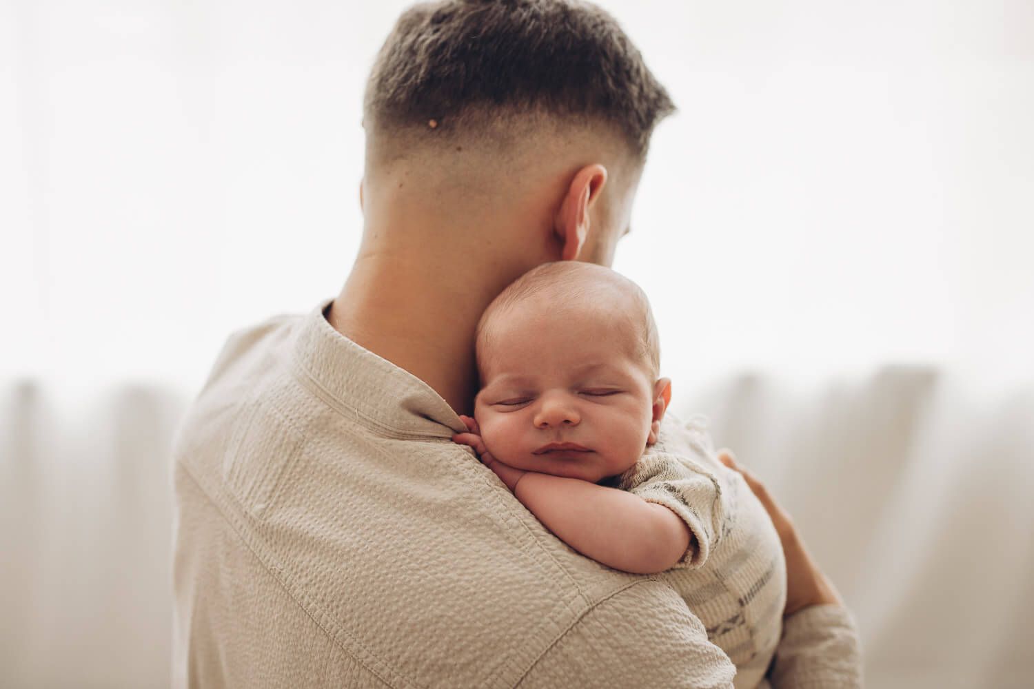 Vater hält sein schlafendes Neugeborenes liebevoll beim Familien Fotoshooting