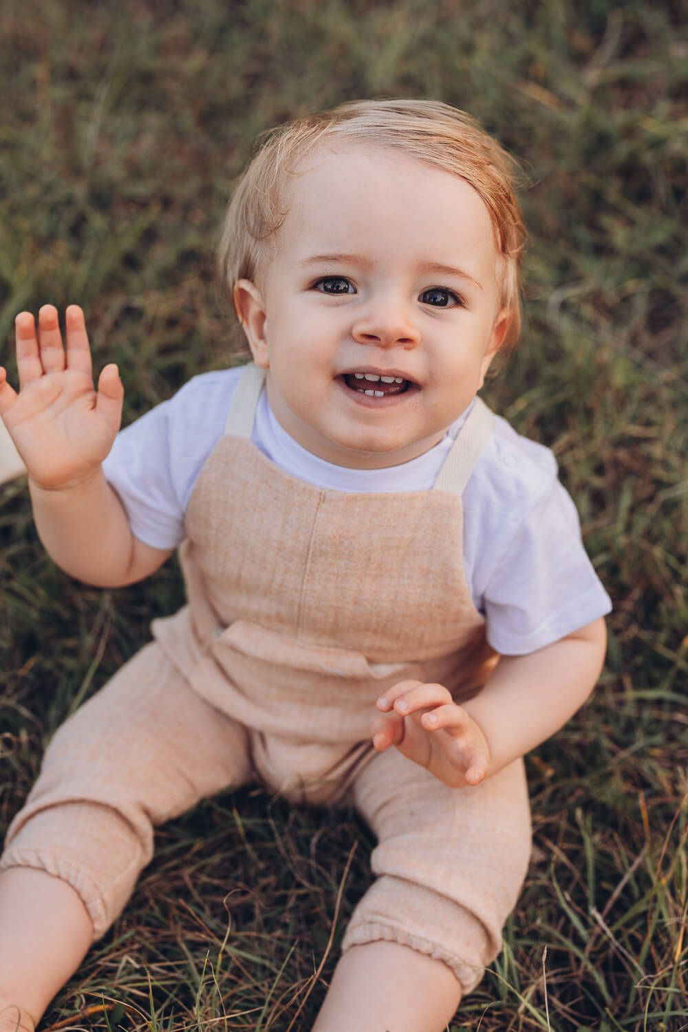 Fröhliches Baby sitzt im Gras und lacht in die Kamera beim natürlichen Outdoorfotoshooting Hannover