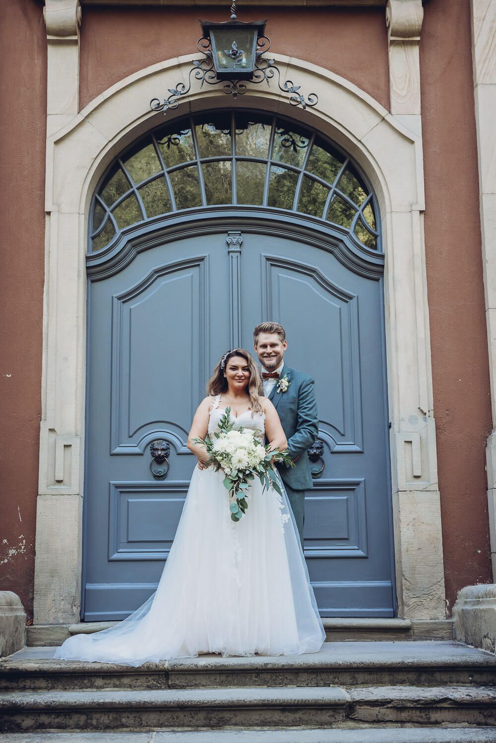 Brautpaar posiert elegant vor einer historischen blauen Eingangstür, fotografiert von einem Hochzeitsfotografen in Hannover