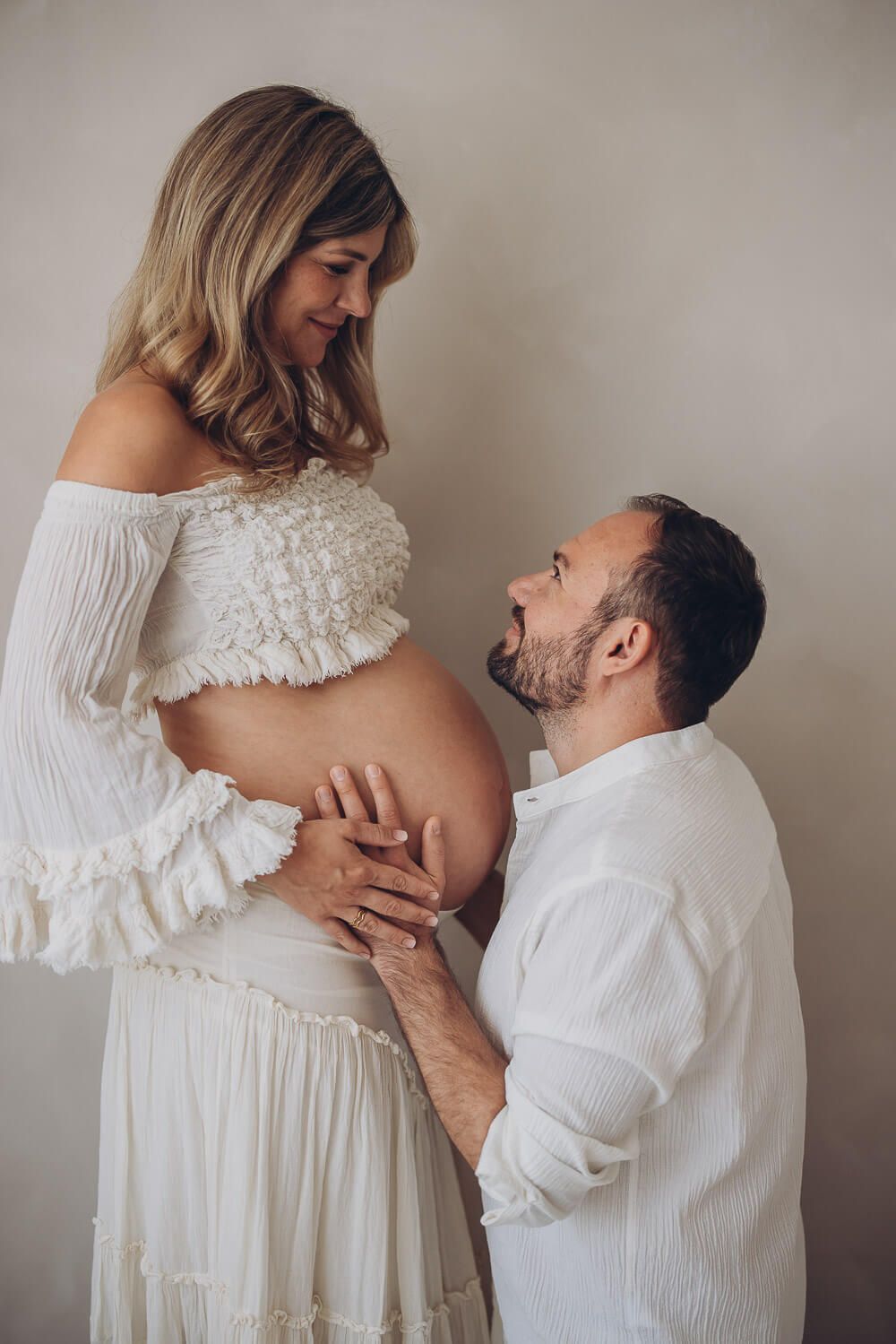 Intimes Babybauch Fotoshooting in Wolfsburg – werdender Vater kniet vor der schwangeren Frau und hält liebevoll ihren Bauch