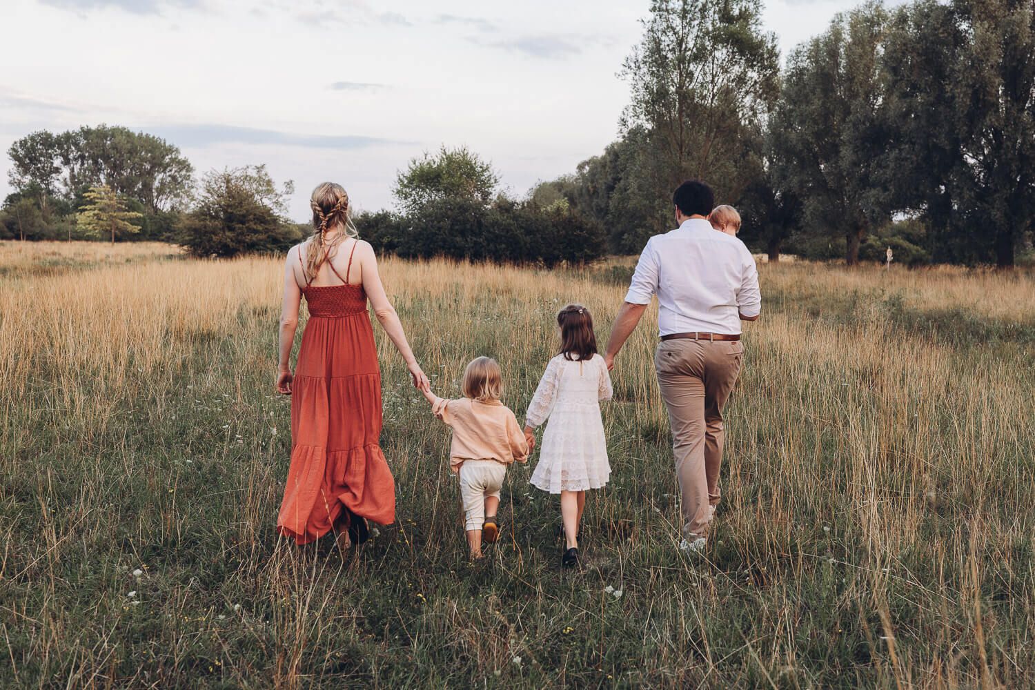 Familie läuft Hand in Hand durch eine Wiese beim Outdoorfotoshooting Wolfsburg, aufgenommen von hinten in natürlicher Szenerie