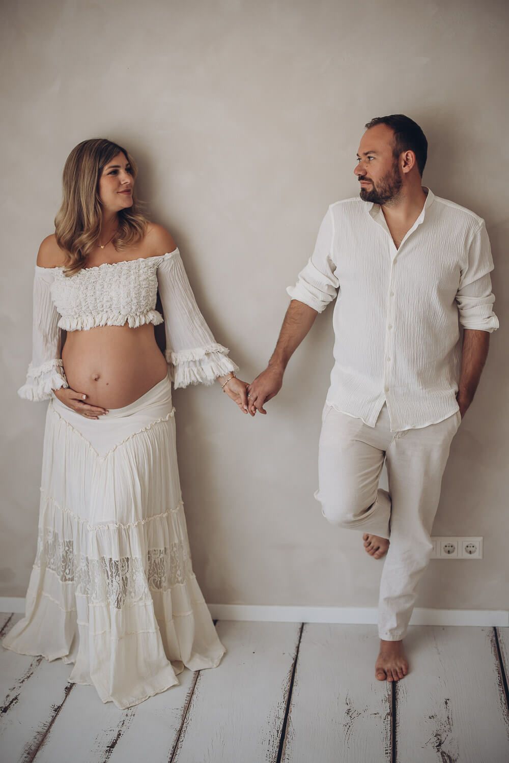 Modernes Babybauch Fotoshooting als Paar in Celle – werdende Eltern stehen an der Wand und halten sich an den Händen