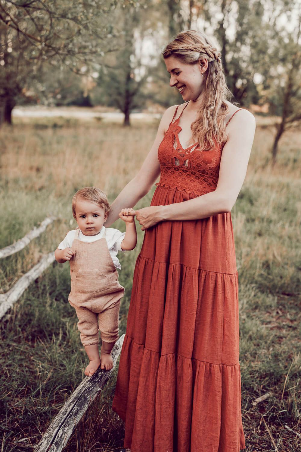 Mutter unterstützt ihr Baby beim Laufen auf einem Baumstamm während eines entspannten Outdoor Shootings in Wolfsburg