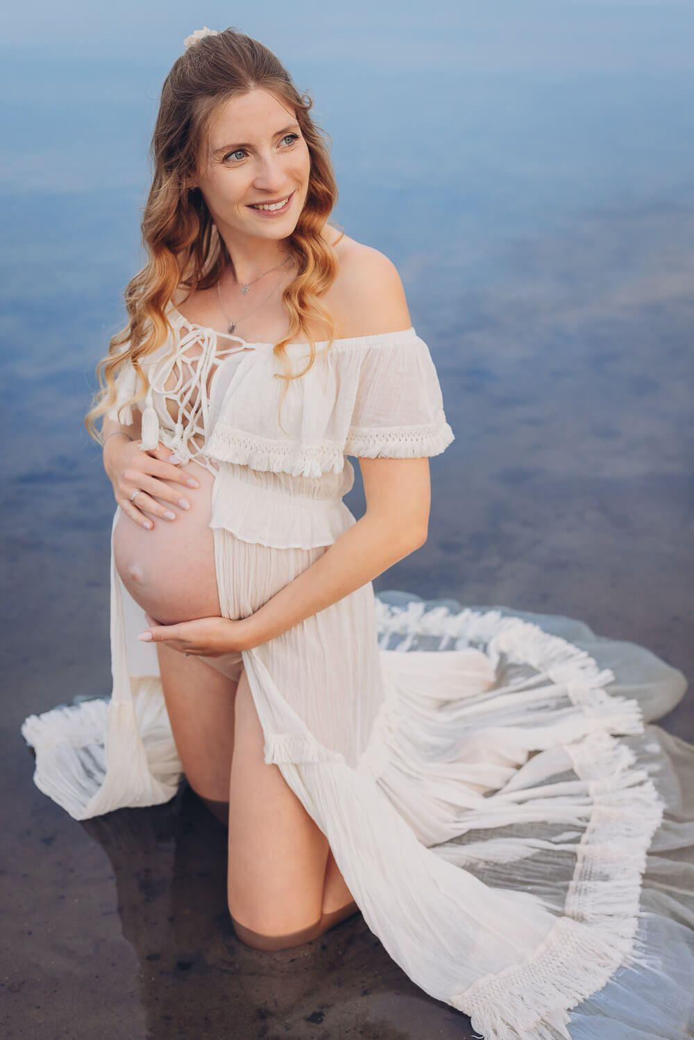 Natürliches Babybauch Fotoshooting im Wasser bei Neustadt am Rübenberge – schwangere Frau kniet im See mit fließendem Kleid