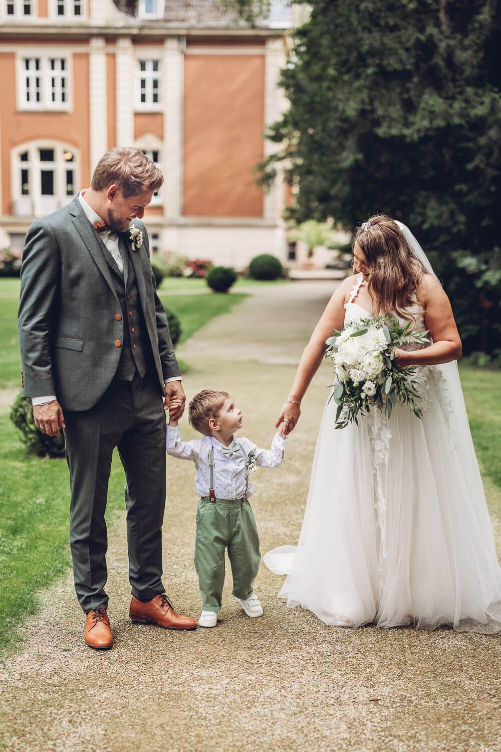 Brautpaar läuft mit seinem Kind Hand in Hand vor der Hochzeitslocation, aufgenommen von einem Hochzeitsfotografen in Garbsen