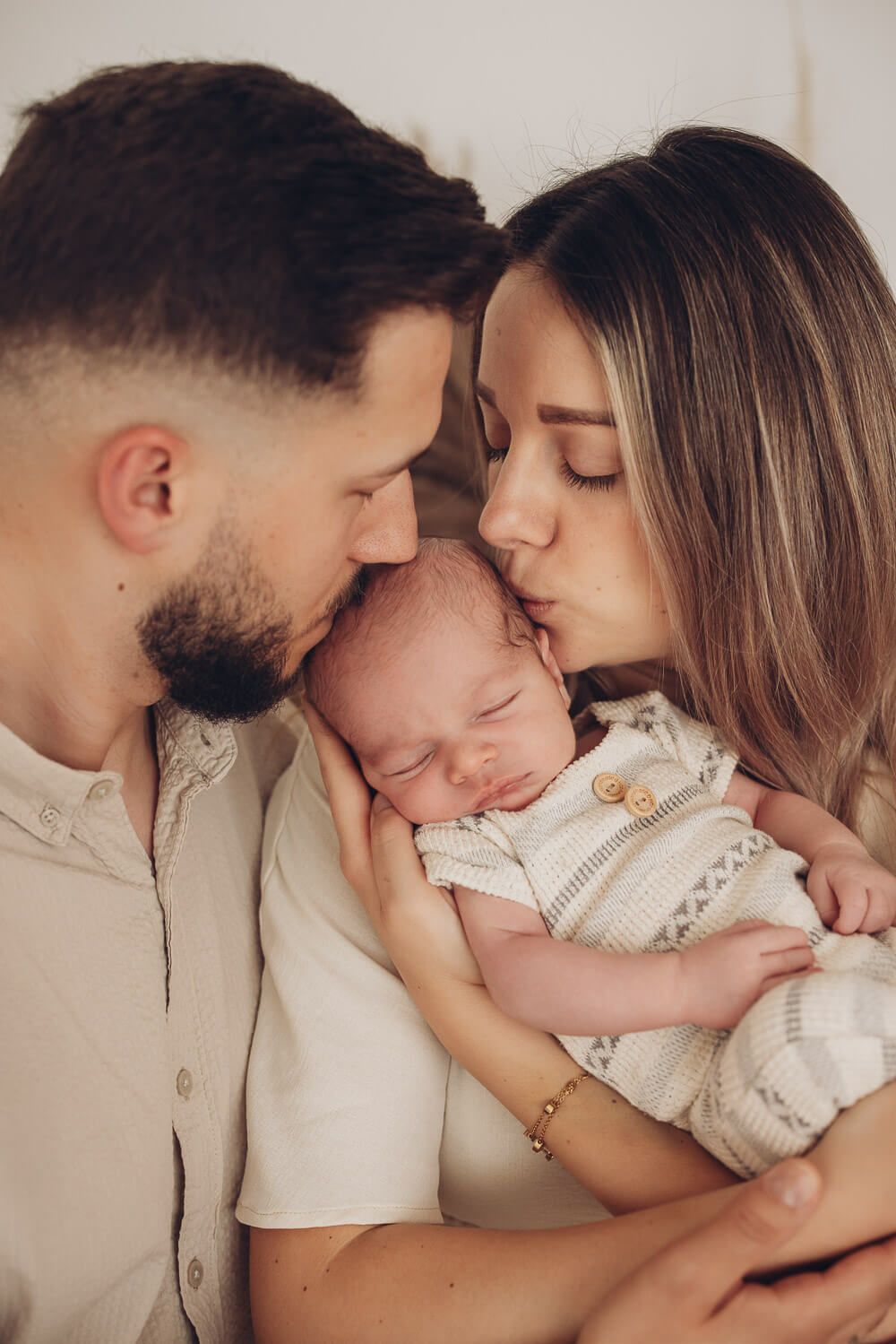 Beide Eltern küssen ihr Neugeborenes liebevoll bei einem warmen Familien Fotoshooting in Hildesheim