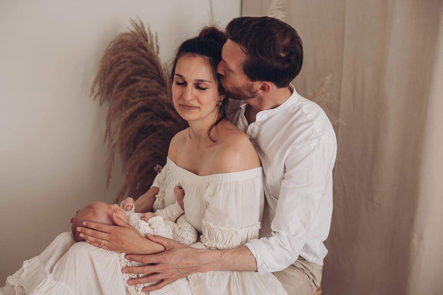 Emotionales Newborn Shooting im Fotostudio nahe Hildesheim, Vater küsst liebevoll die Mutter während sie ihr Baby im Arm hält