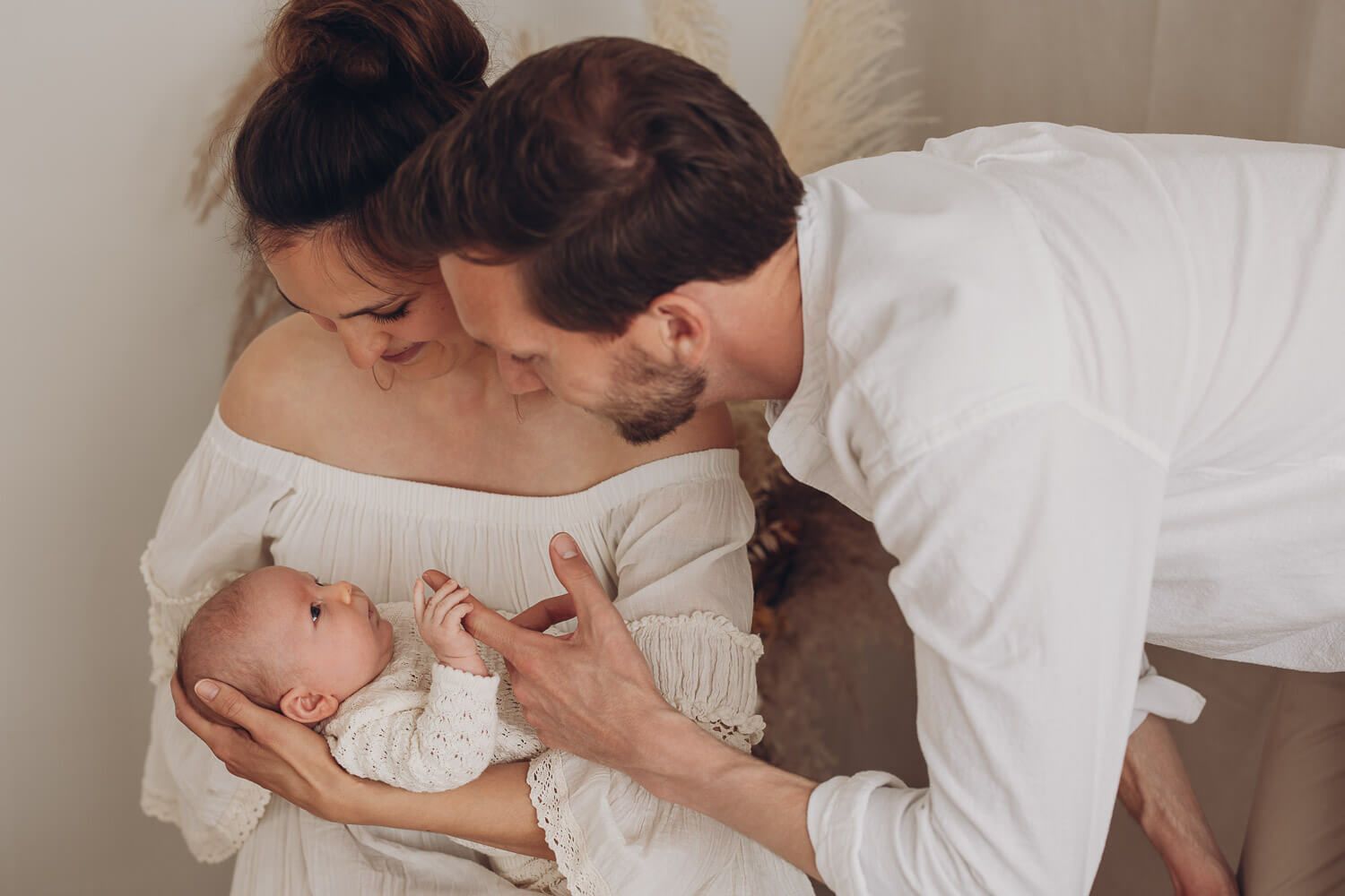 Innige Familienszene im Fotostudio Hannover, Eltern beugen sich gemeinsam über ihr Neugeborenes und schenken ihm Aufmerksamkeit