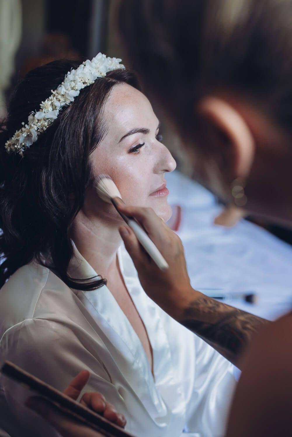 Eine Stylistin trägt der Braut behutsam Make-up auf, während sie sich auf ihre freie Trauung in Minden vorbereitet - Hochzeitsfotograf