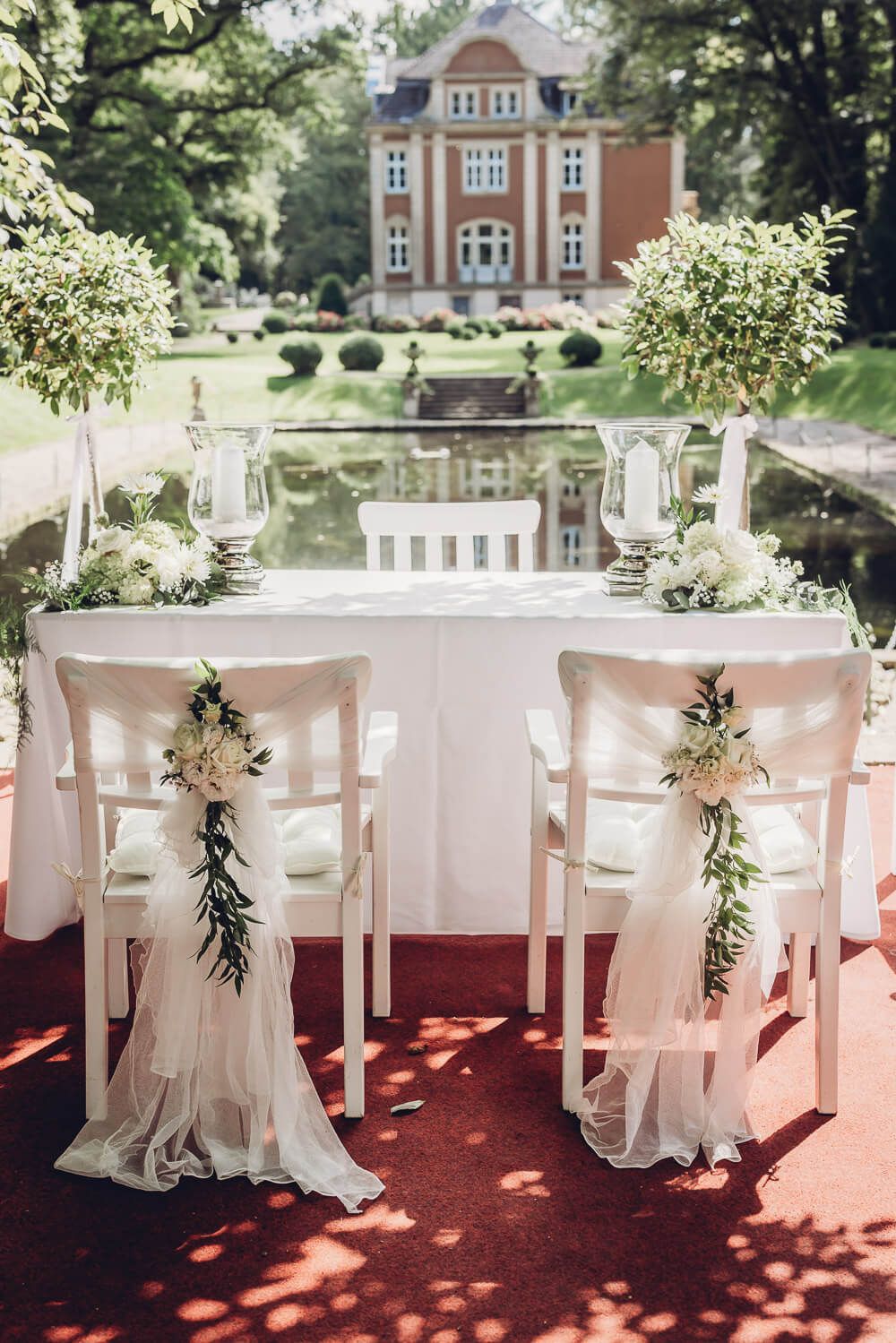 Dekorierter Trauplatz mit weißen Stühlen, Blumen und Blick auf eine Villa bei Hannover - Hochzeitsfotograf Celle