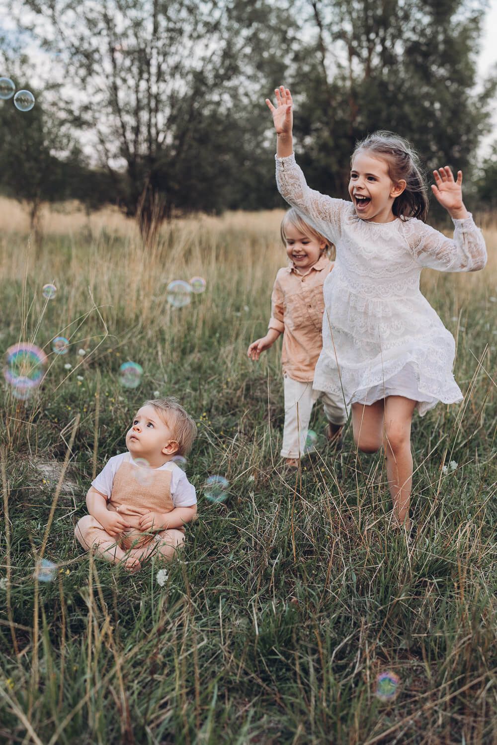 Kinder rennen lachend durch eine Wiese und spielen mit Seifenblasen beim lebendigen Outdoorfotoshooting Hannover