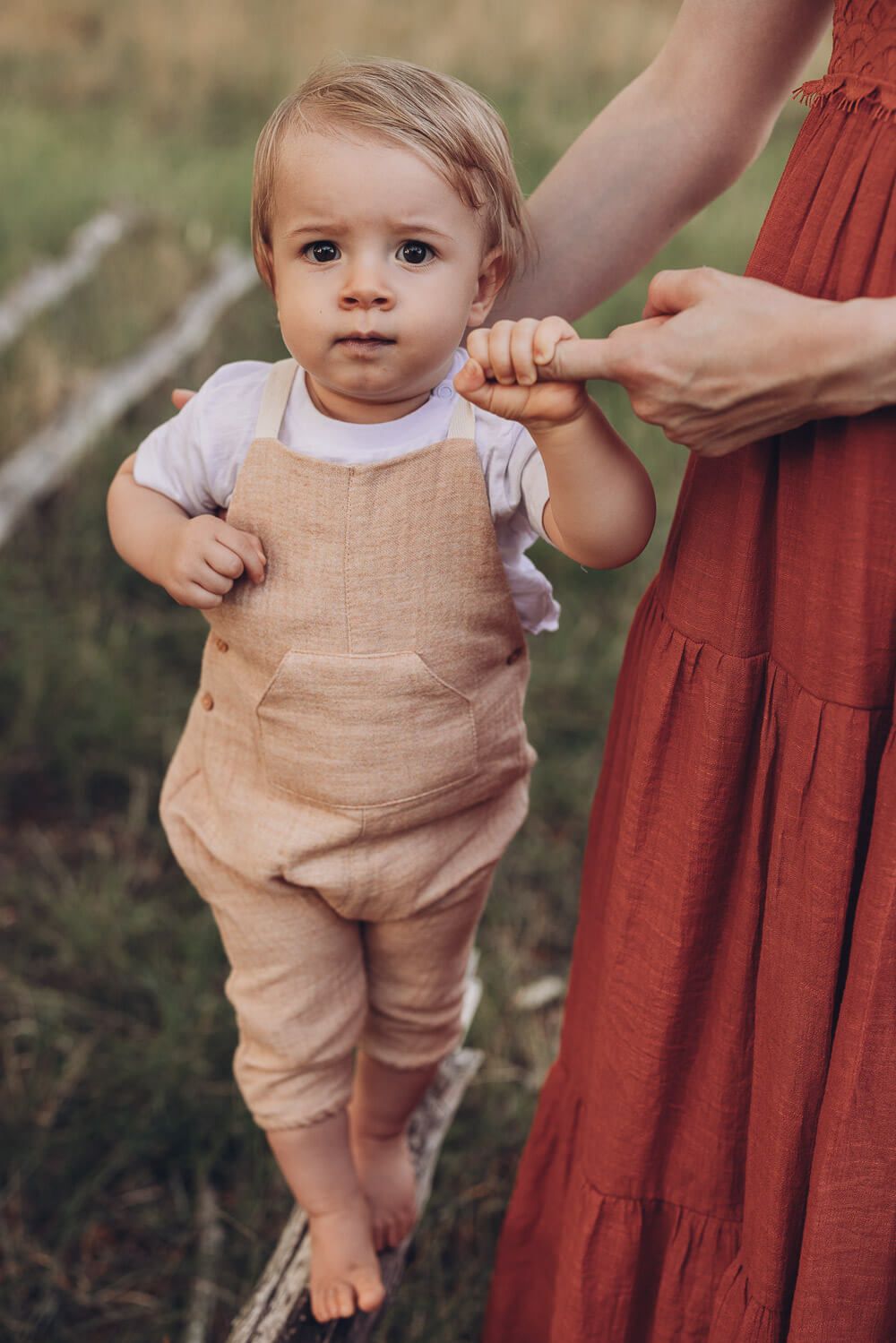 Kleinkind balanciert vorsichtig auf einem Baumstamm beim Outdoorfotoshooting Hannover und wird dabei von der Mutter gehalten