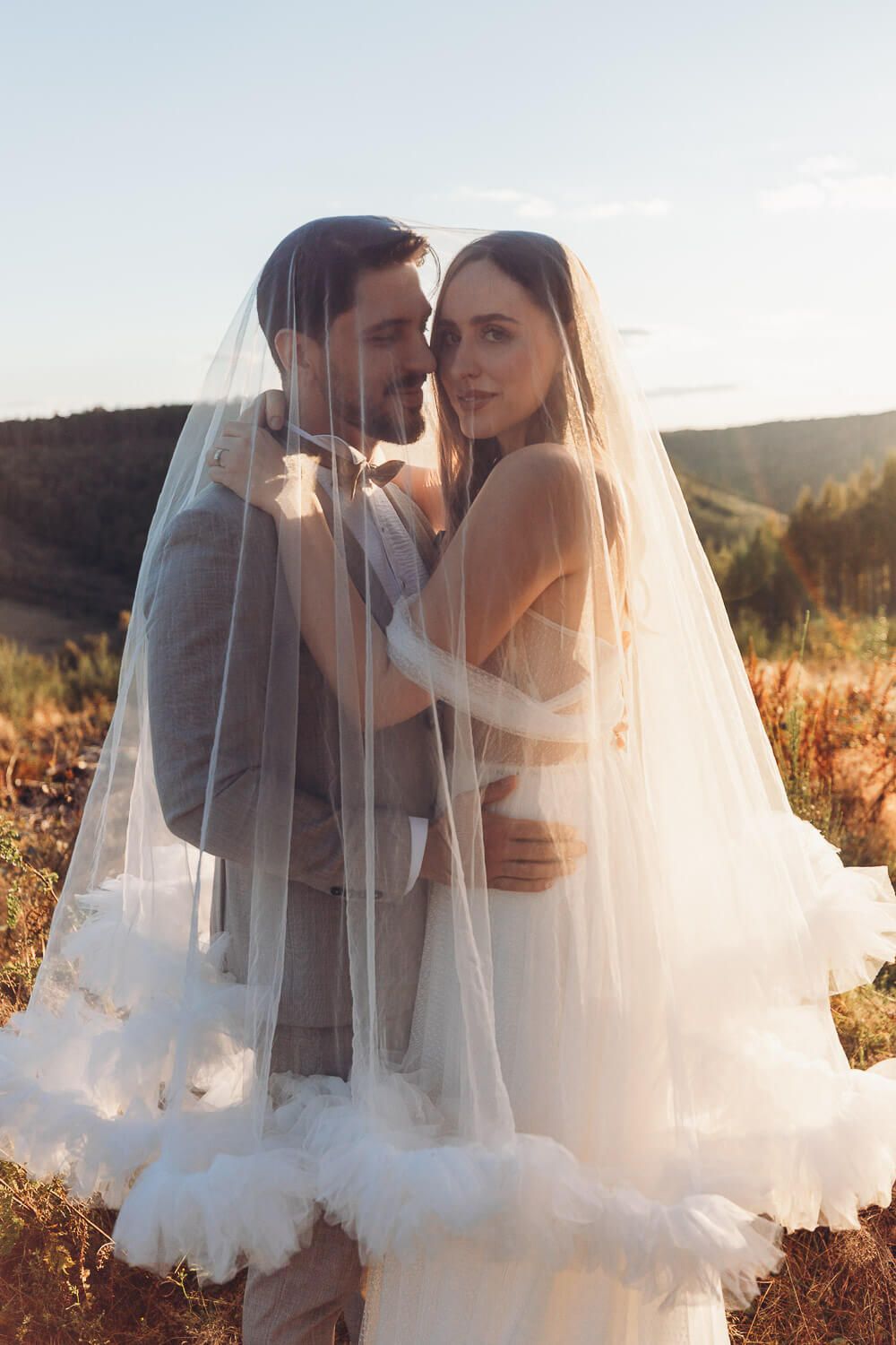 Braut und Bräutigam stehen eng umschlungen unter einem zarten Schleier im weichen Abendlicht bei einem Hochzeitsshooting in Minden