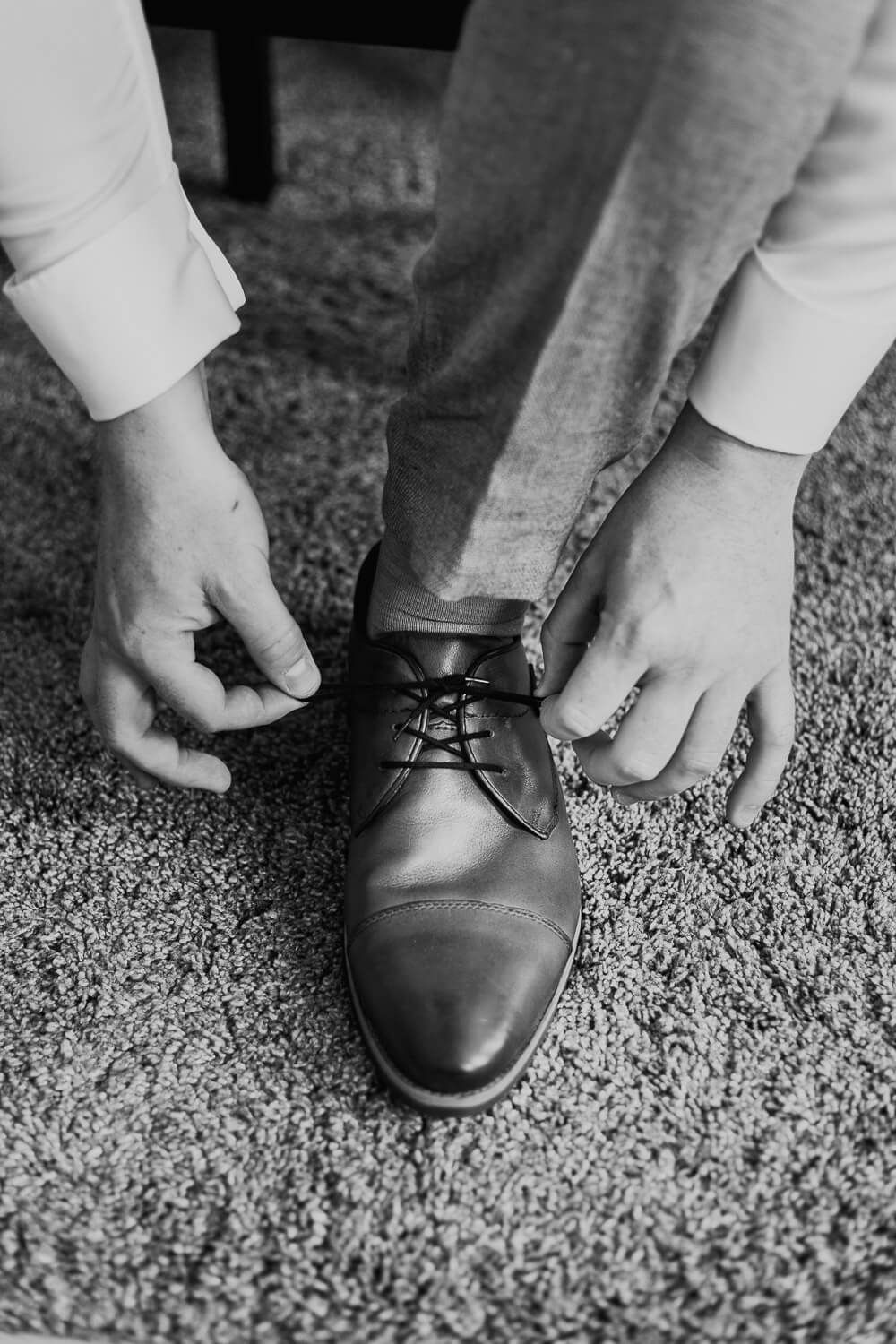 Schwarzweiß-Detailaufnahme vom Schuhebinden des Bräutigams beim Getting Ready, fein beobachtet von einem Hochzeitsfotografen