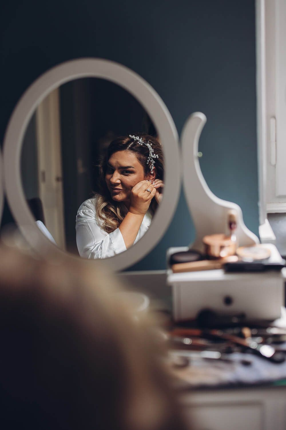 Braut legt beim Getting Ready ihren Ohrring vor dem Spiegel an, stilvoll festgehalten von einem Hochzeitsfotografen in Braunschweig