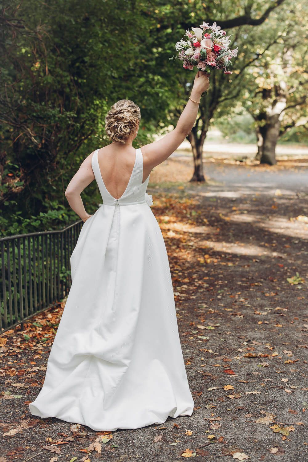 Moderne Braut im eleganten Hochzeitskleid hält ihren Strauß hoch bei einem kreativen Fotoshooting eines Hochzeitsfotografen aus Hannover