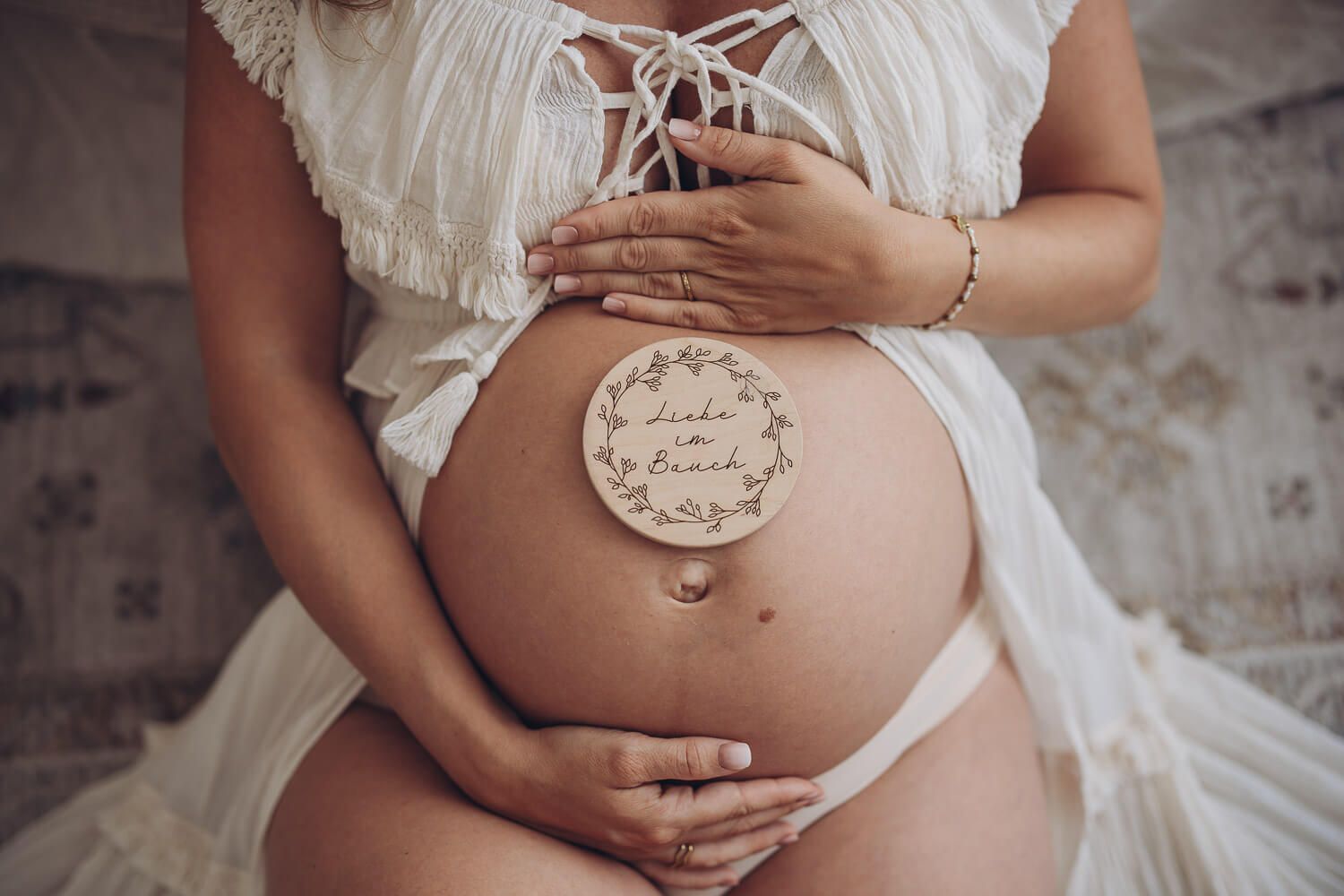 Detailaufnahme beim Babybauch Fotoshooting in Langenhagen – Hände umrahmen den Bauch mit Holzschild „Liebe im Bauch“