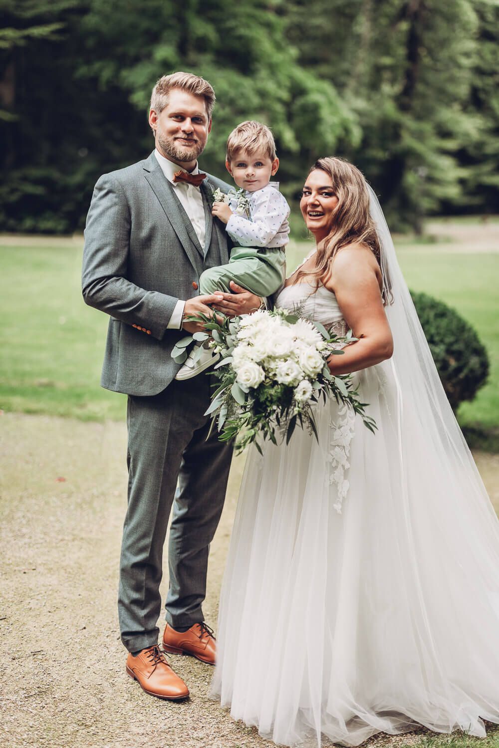 Liebevolles Familienfoto von Brautpaar und Kind im Grünen am Hochzeitstag, fotografiert von einem Fotografen in Braunschweig