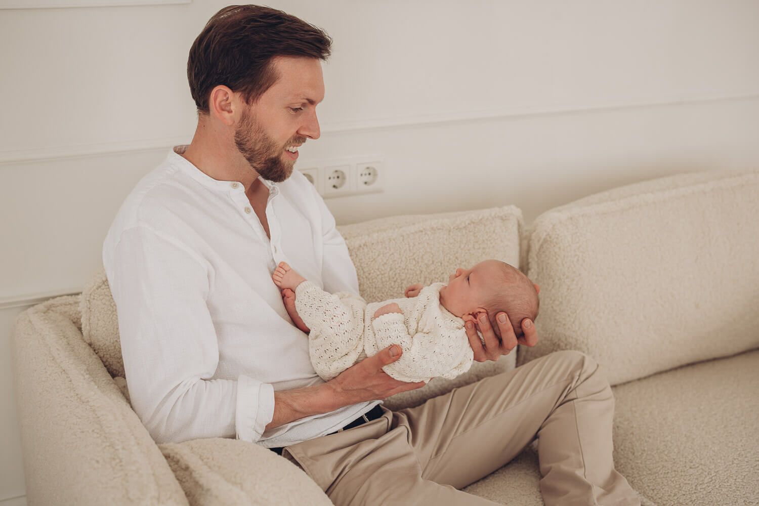 Authentische Szene im Fotostudio Hannover, Vater sitzt entspannt auf dem Sofa und hält sein Baby liebevoll im Arm