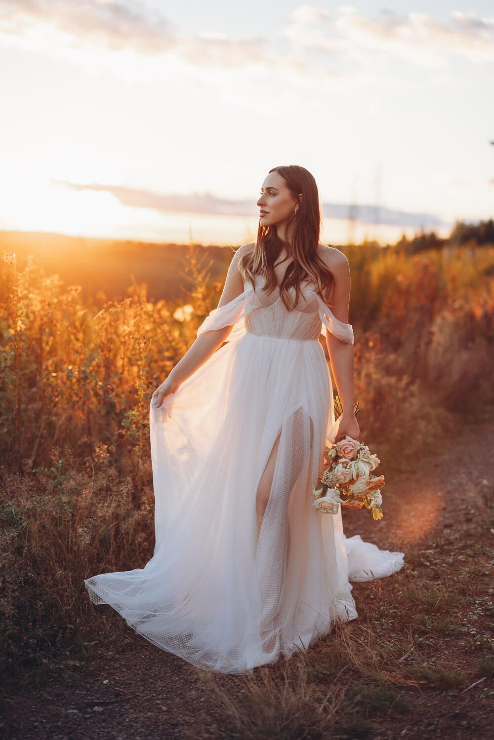Braut mit wallendem Kleid und Blumenstrauß steht im goldenen Abendlicht auf einem Naturweg bei einem Hochzeitsshooting in Celle