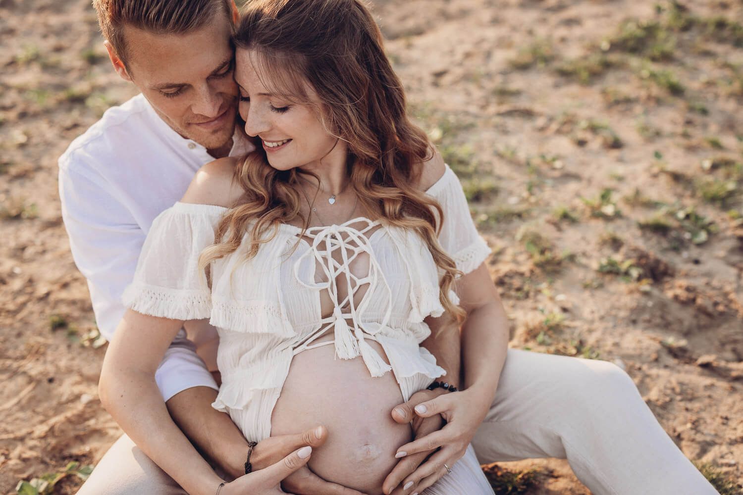 Paar sitzt zusammen und legt gemeinsam die Hände auf den Babybauch in einer intimen Nahaufnahme - Outdoorshooting Hannover