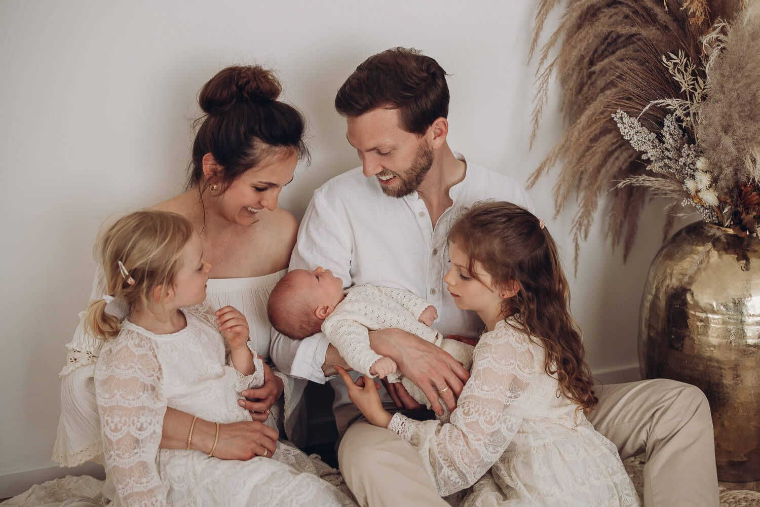 Familienfoto im Fotostudio bei Wolfsburg, Eltern und Geschwisterkinder schauen aufmerksam und liebevoll auf das Baby