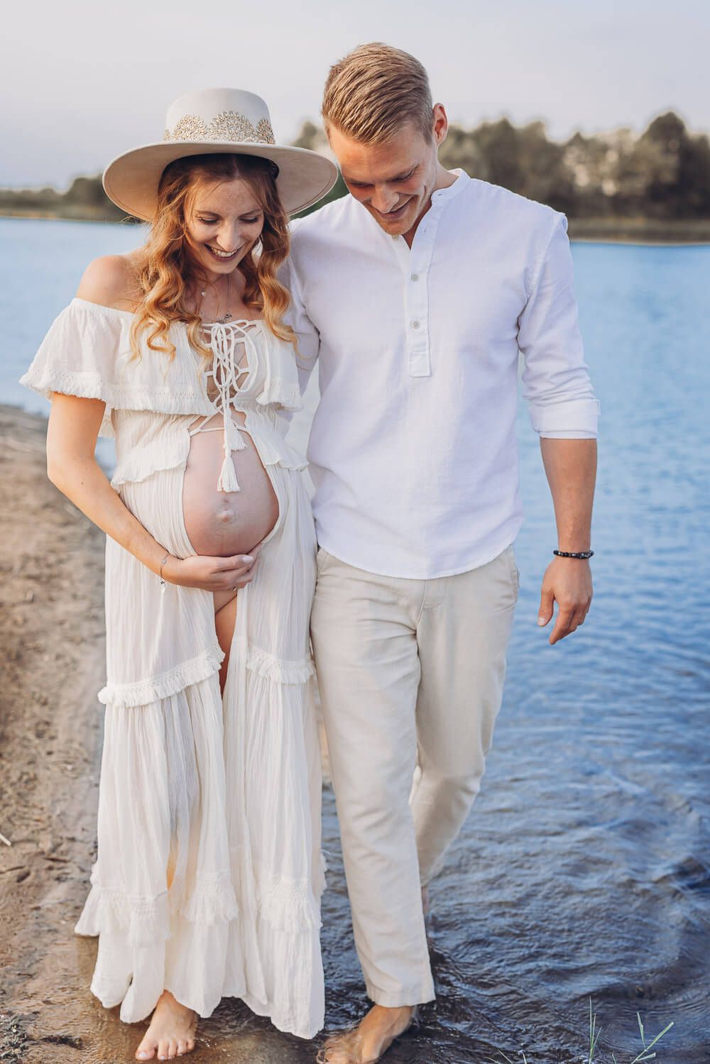 Babybauch Fotoshooting am See bei Celle – Paar spaziert am Wasser und hält liebevoll den Babybauch