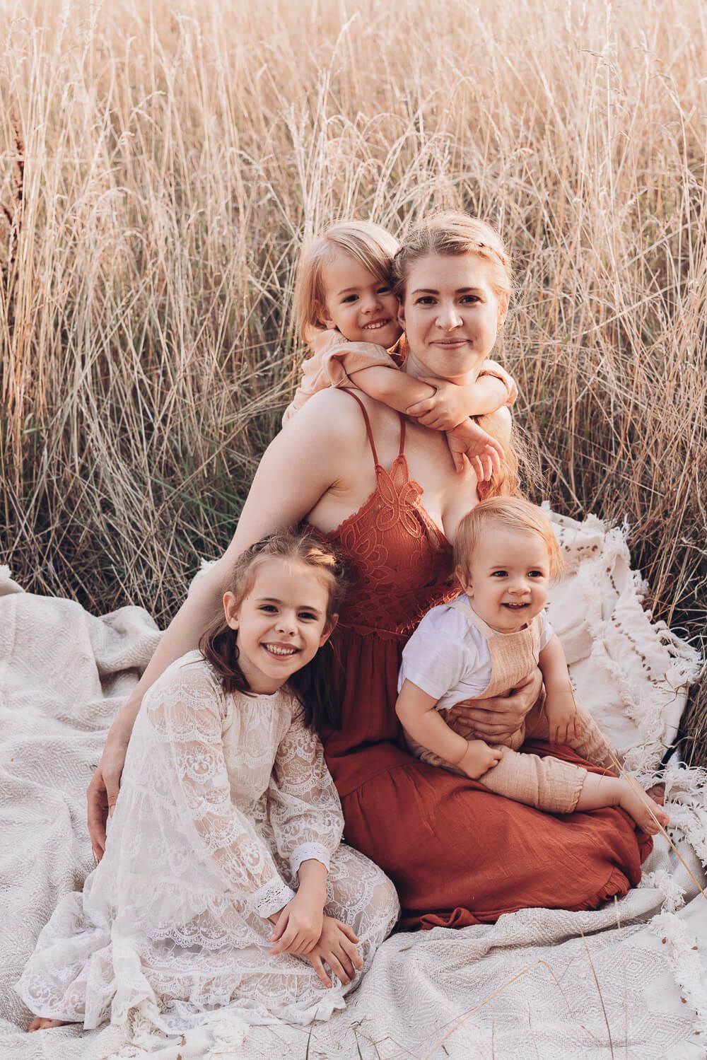 Liebevoller Moment beim Outdoorfotoshooting Hannover, Mutter sitzt mit ihren Kindern im hohen Gras und alle lächeln in die Kamera