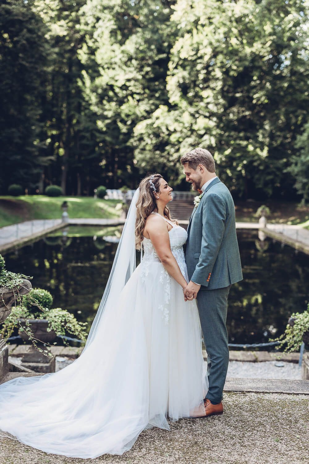 Romantisches Brautpaar steht Hand in Hand vor einem Teich im Grünen, aufgenommen von einer Hochzeitsfotografin in Celle