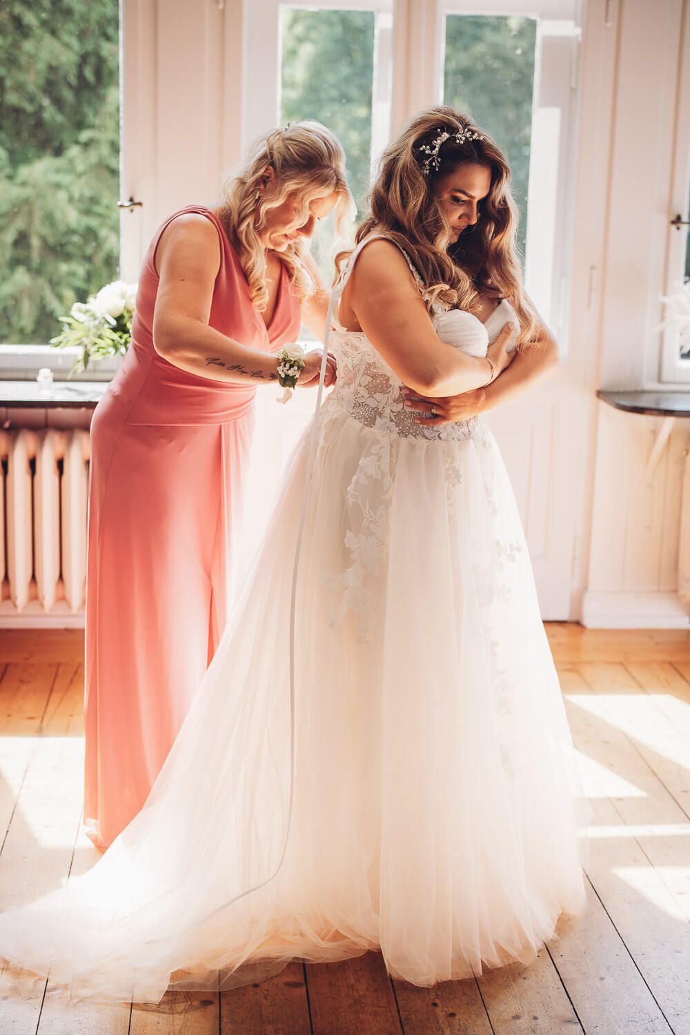 Braut wird von Trauzeugin in einer schöner Hochzeitsvilla angezogen - Hochzeitsfotograf Hannover