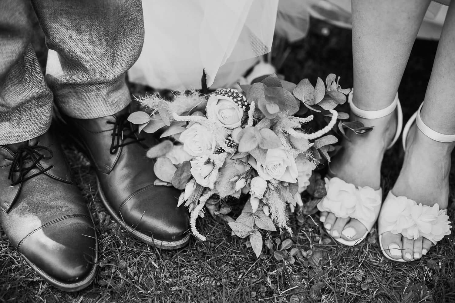 Schwarz-Weiß-Detailaufnahme von Brautschuhen, Bräutigamschuhen und Brautstrauß bei einer Hochzeit in Pattensen