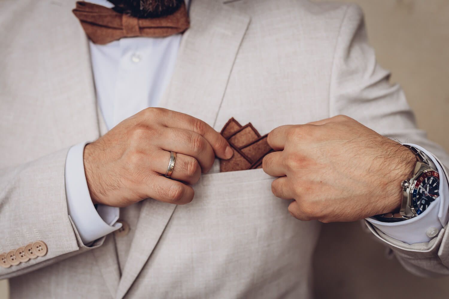 Detailaufnahme eines Bräutigams im Anzug mit Einstecktuch, Ehering und Armbanduhr, fotografiert von einem Hochzeitsfotografen in Hannover